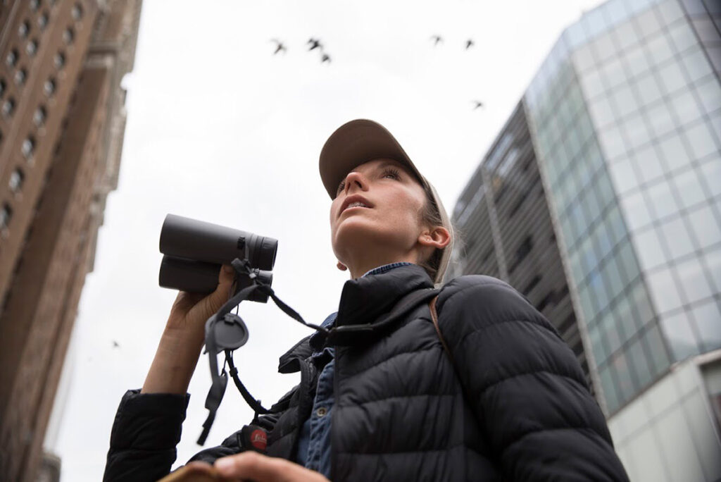 Birder and gardener Annie Novak looks skyward in New York City, holding her binoculars in one hand, photo by Sophie Butcher.