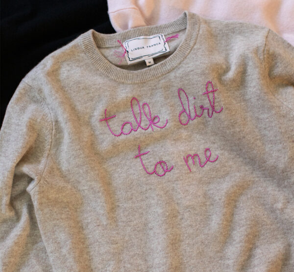 A Lingua Franca x Perfect Earth Project collaboration featuring a beige cashmere sweater with fuchsia embroidery that says 'Talk Dirt to Me.'