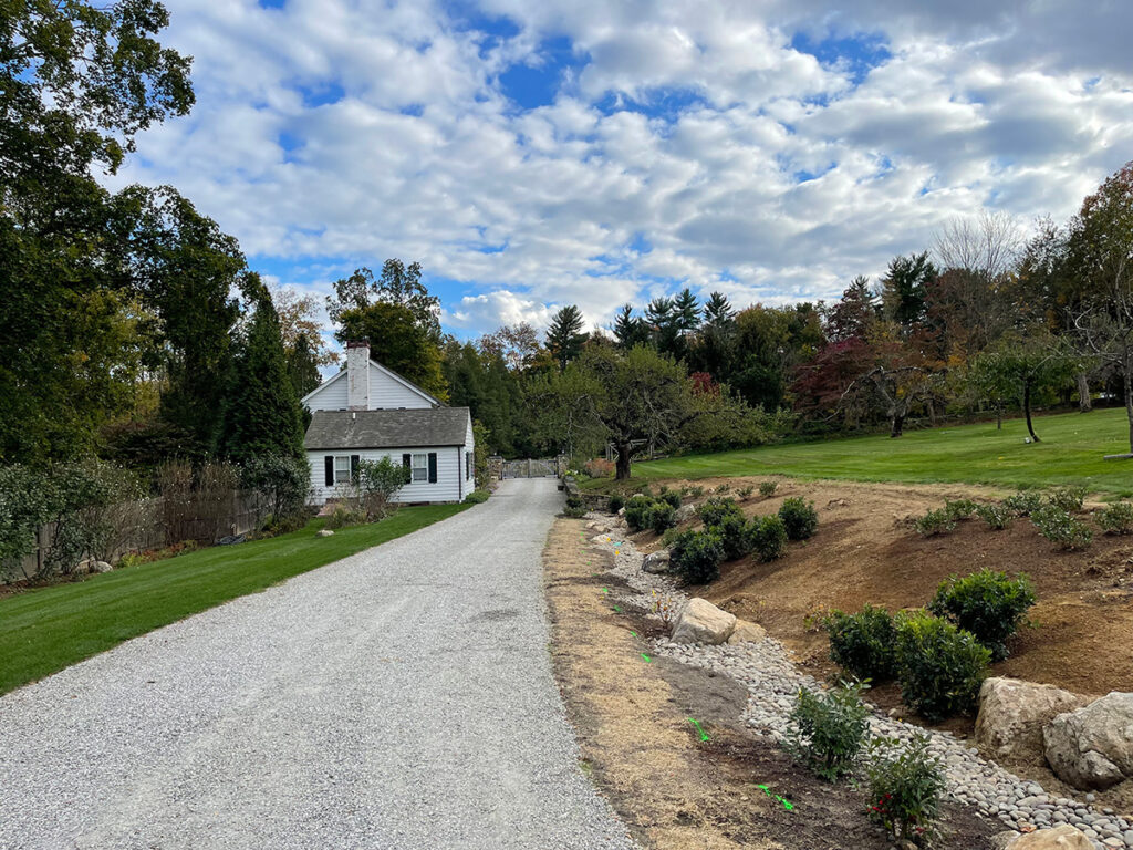 A behind-the-scenes view of a swale in the process of being planted, which includes native shrubs and a rock "river bed."
